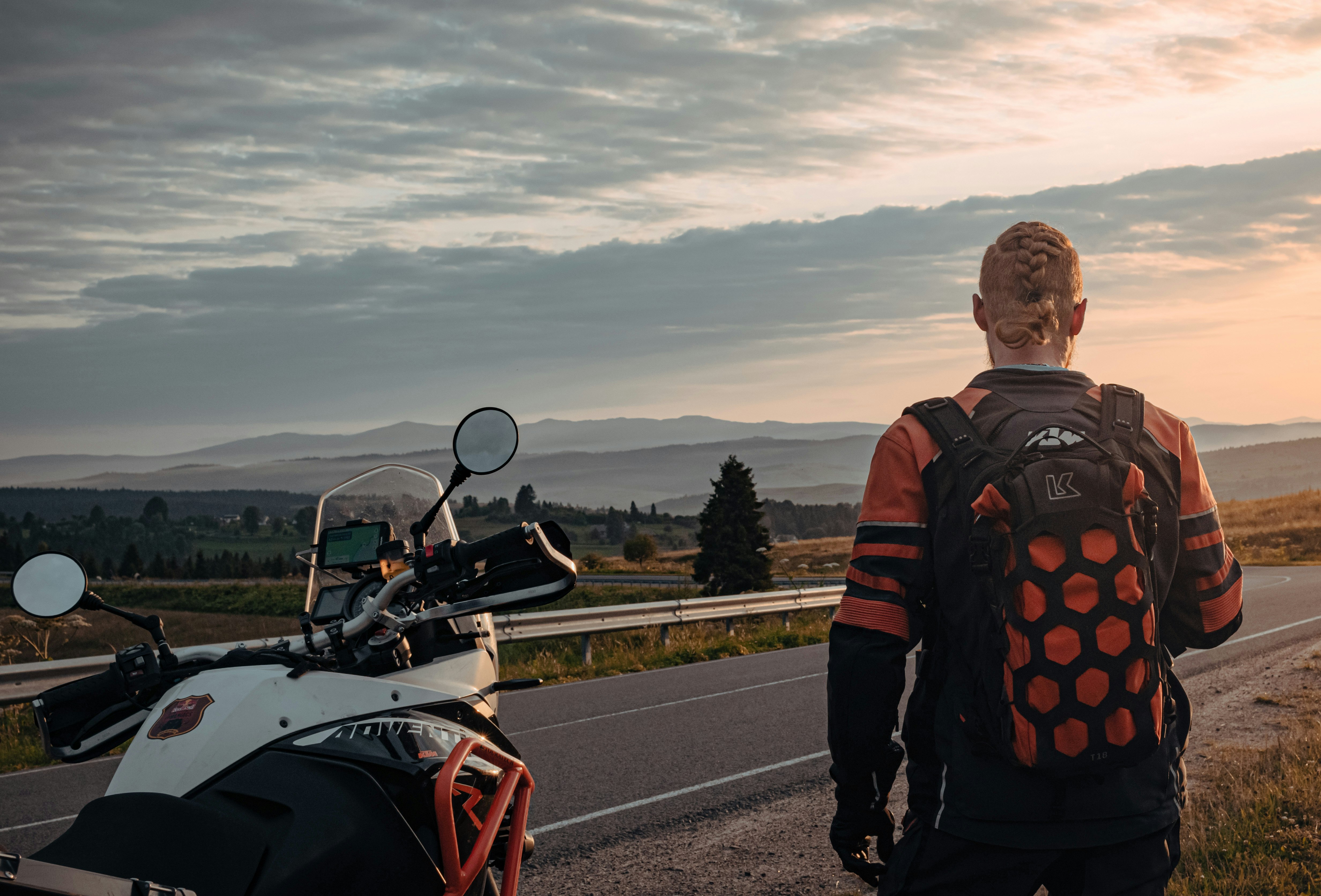 man in black and orange jacket standing beside red and black motorcycle during daytime